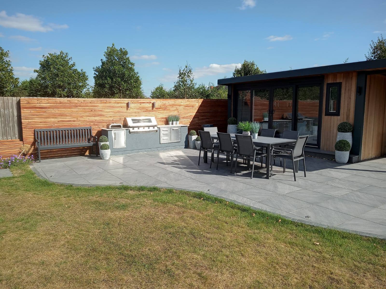 Luxury outdoor dining area with built-in BBQ kitchen, porcelain paving and garden room by Cornerstone