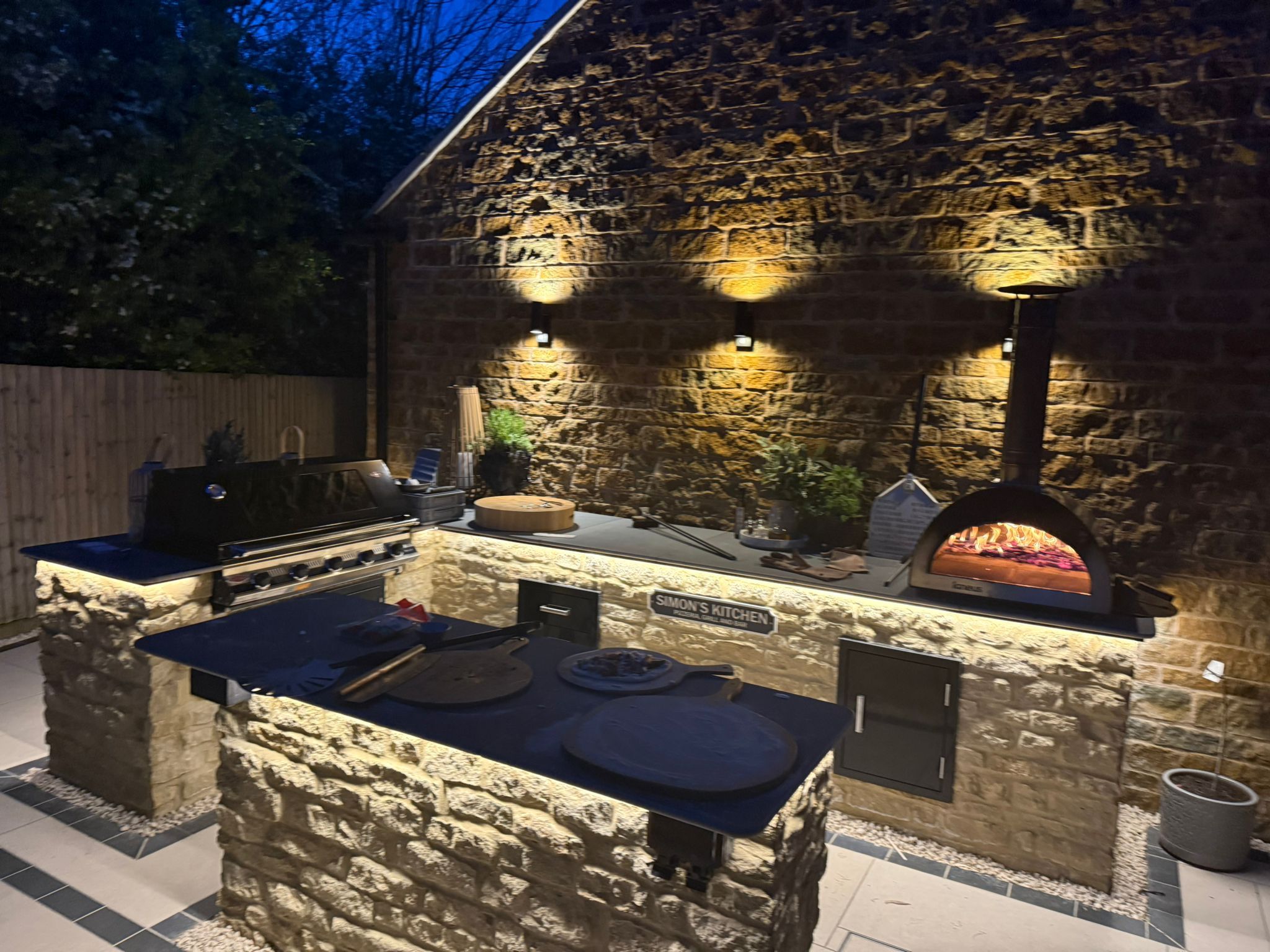 Illuminated outdoor kitchen and entertainment area by Cornerstone Landscape Services
